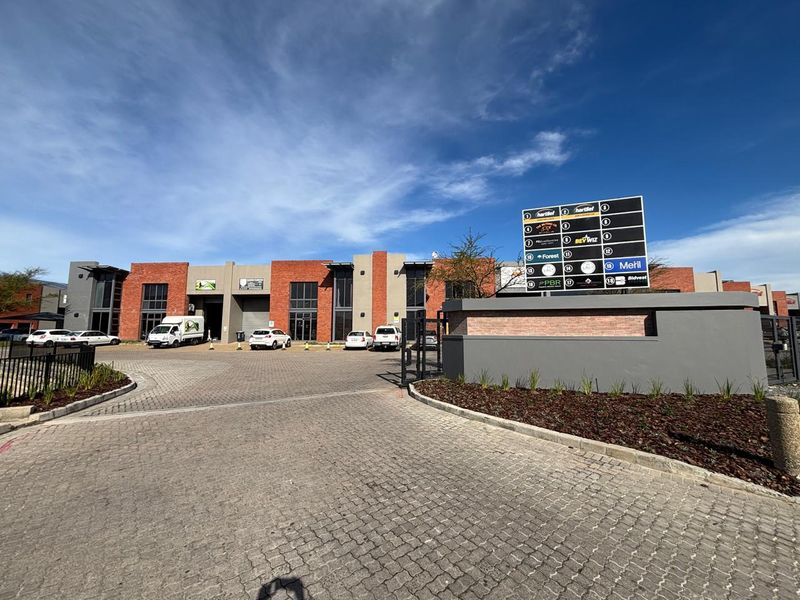 Front view of a modern industrial business park featuring brick facade units, paved driveway, and a prominent commercial directory signage board.