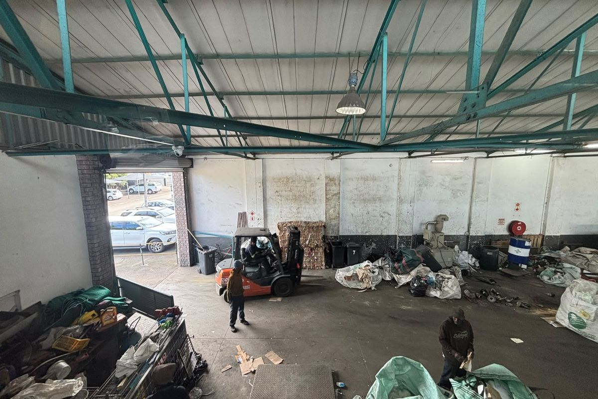 Spacious industrial warehouse area featuring exposed steel roof trusses, concrete flooring, and a large roller shutter door for vehicle access.