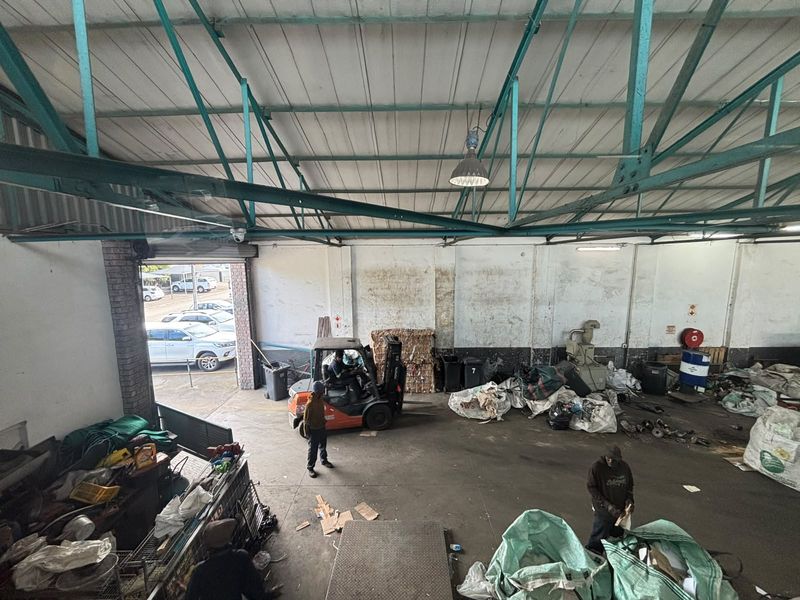 Spacious industrial warehouse area featuring exposed steel roof trusses, concrete flooring, and a large roller shutter door for vehicle access.