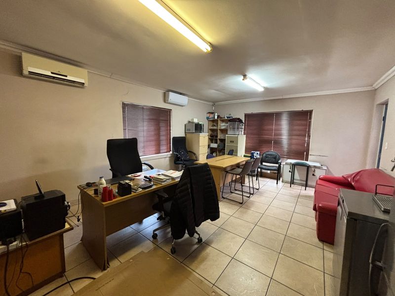 A functional office space featuring tiled flooring, dual split-system air conditioning units, and venetian blinds, providing a practical work environment.
