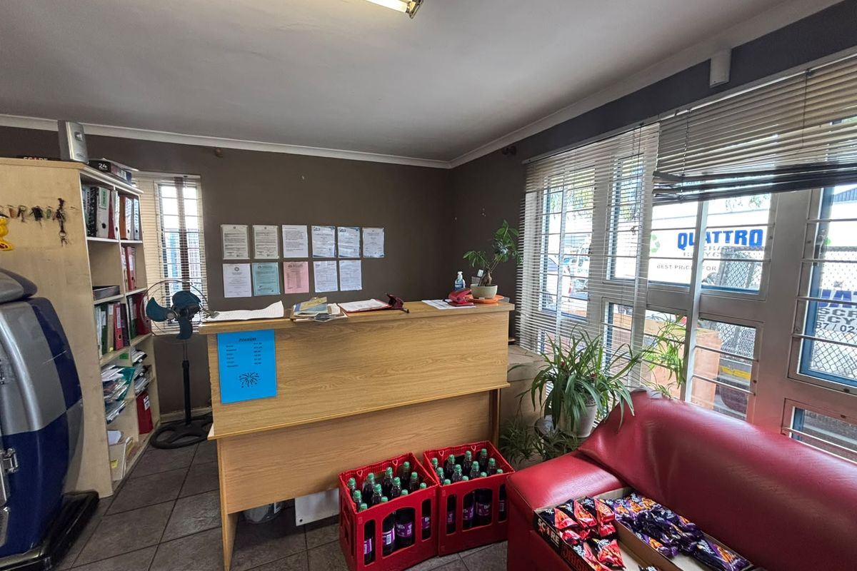 Functional office space featuring tiled flooring, built-in shelving, and large windows with venetian blinds, suitable for administrative or reception use.