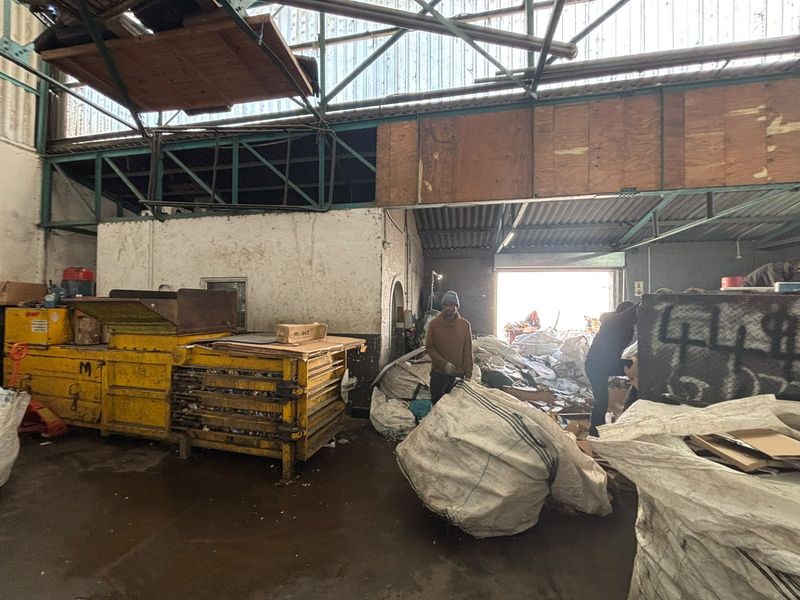 Industrial utility space featuring exposed steel roof trusses, concrete flooring, and a large roller shutter door, currently utilized for storage and processing.
