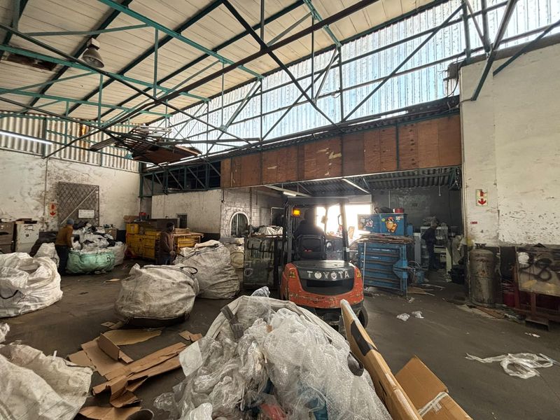 Industrial warehouse space featuring high ceilings with exposed steel trusses, concrete flooring, and functional lighting, currently utilized for storage and operations.