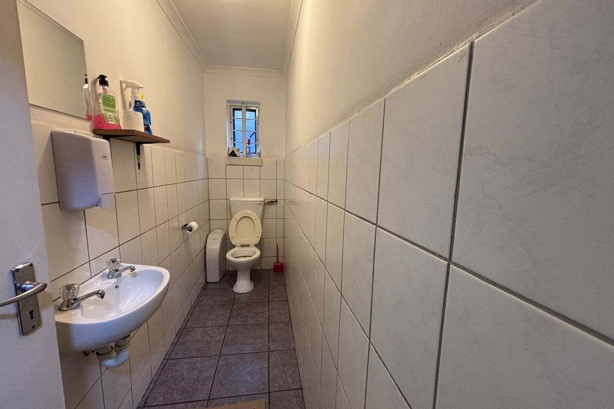 A functional industrial-style restroom featuring a wall-mounted basin, toilet, and full-height ceramic wall tiling.