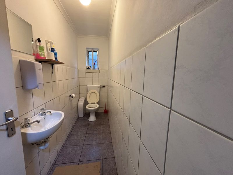 A functional industrial-style restroom featuring a wall-mounted basin, toilet, and full-height ceramic wall tiling.
