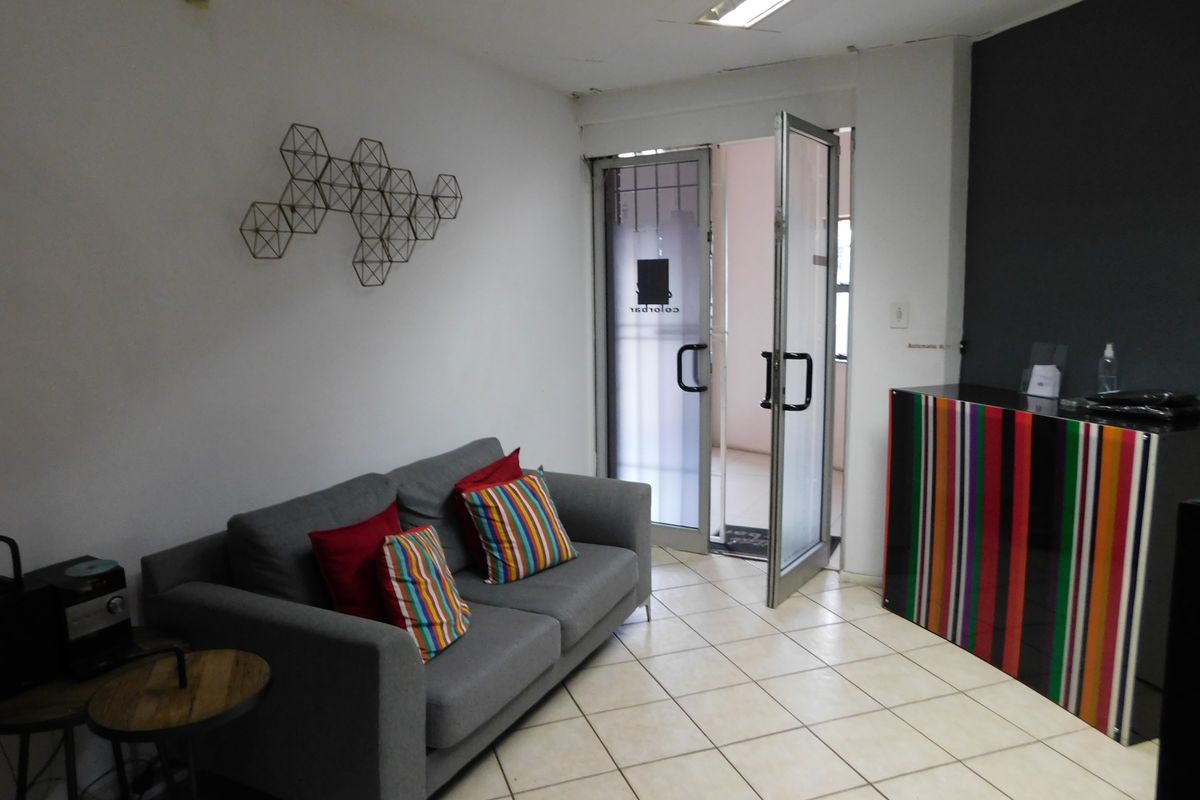 A functional office reception area featuring tiled flooring, fluorescent lighting, and a glass entrance door with security gate.