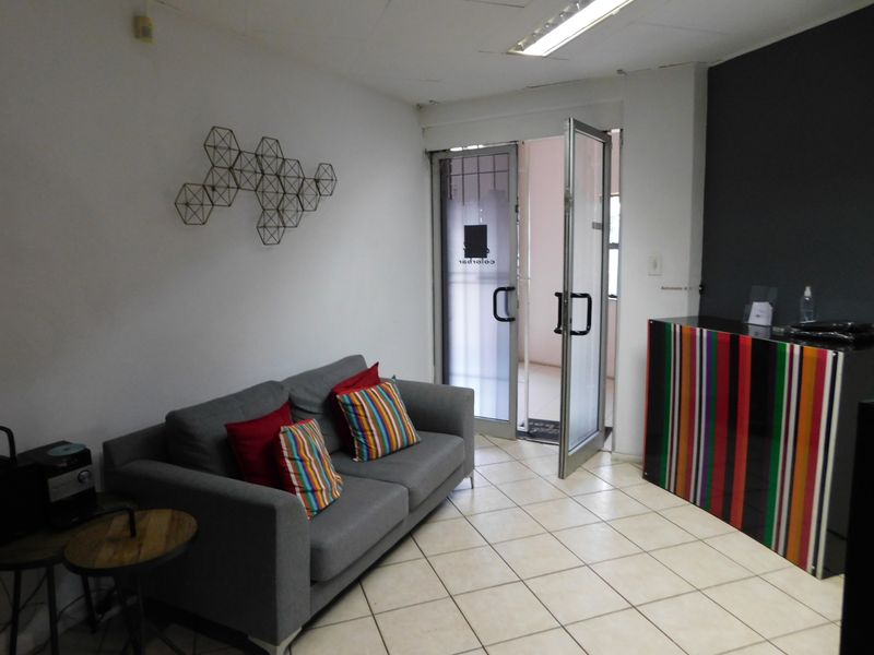 A functional office reception area featuring tiled flooring, fluorescent lighting, and a glass entrance door with security gate.