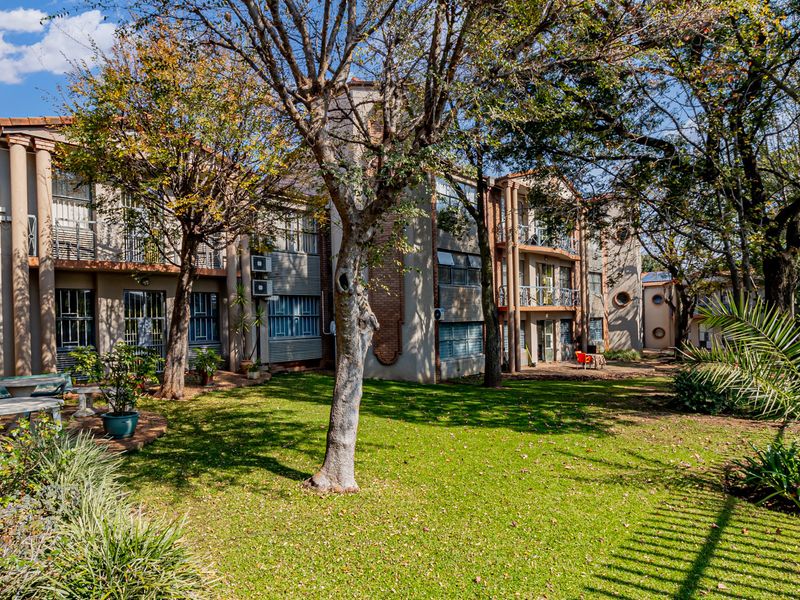 A view of the rear exterior of the office building, featuring a well-maintained garden, mature trees, and accessible ground-floor patio spaces.
