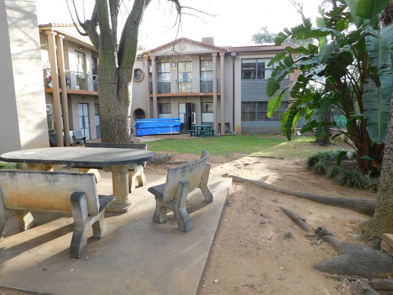 Rear exterior view of the office building featuring a communal concrete patio area, landscaped garden, and multi-level building facade with security features.