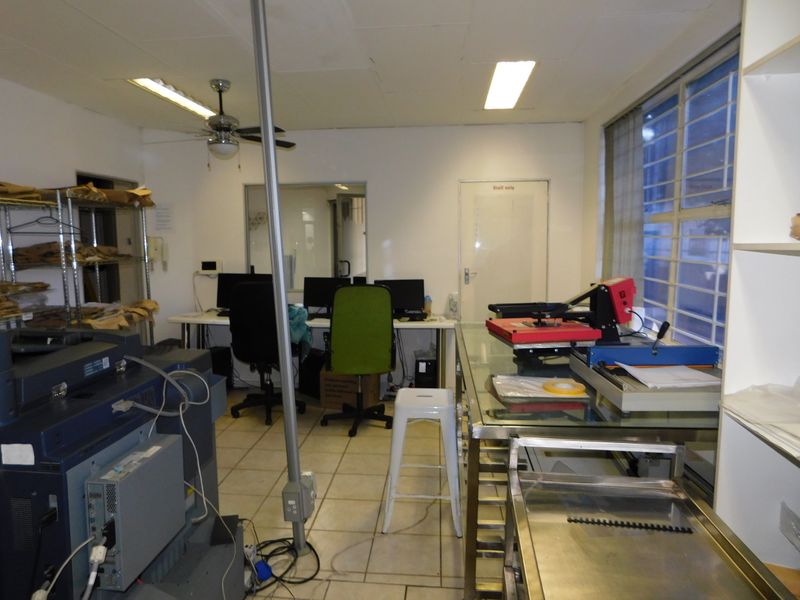Functional office space featuring tiled flooring, built-in shelving, and security bars on windows, suitable for administrative or production use.