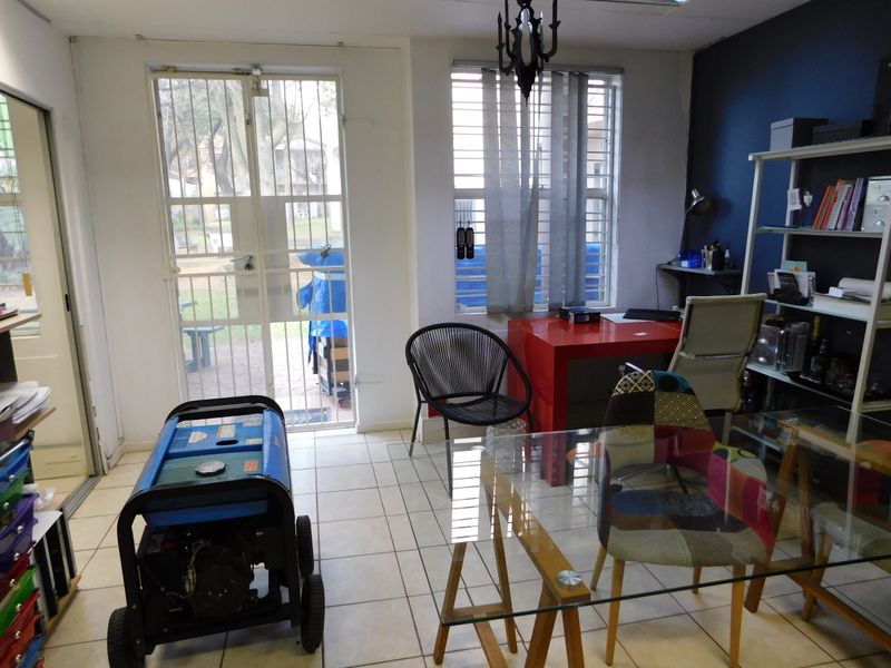 A functional office space featuring ceramic tiled flooring, security gate access, and large windows with vertical blinds, providing natural light and exterior views.