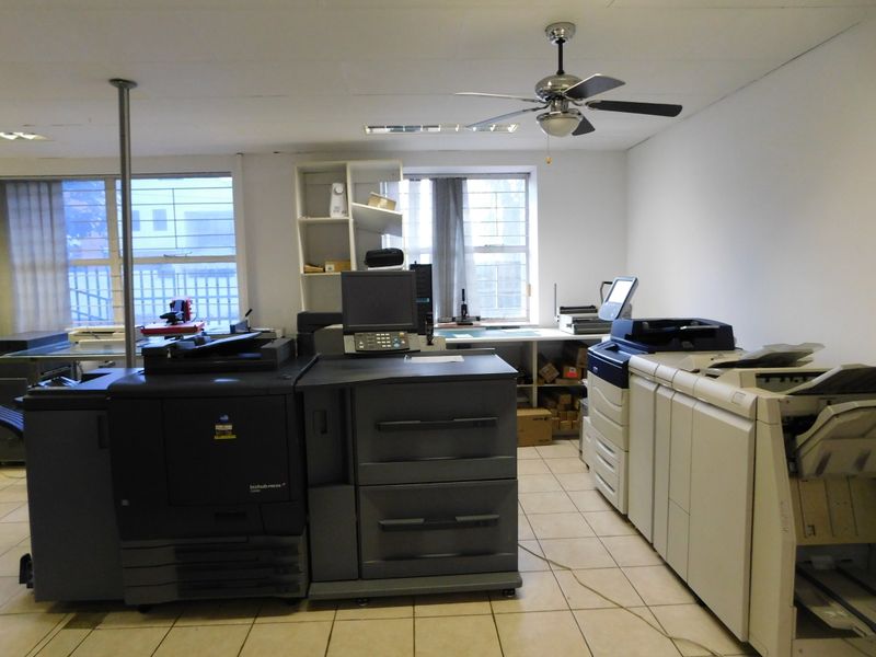 Functional office space featuring tiled flooring, built-in shelving, and a ceiling fan, suitable for a printing or administrative work environment.