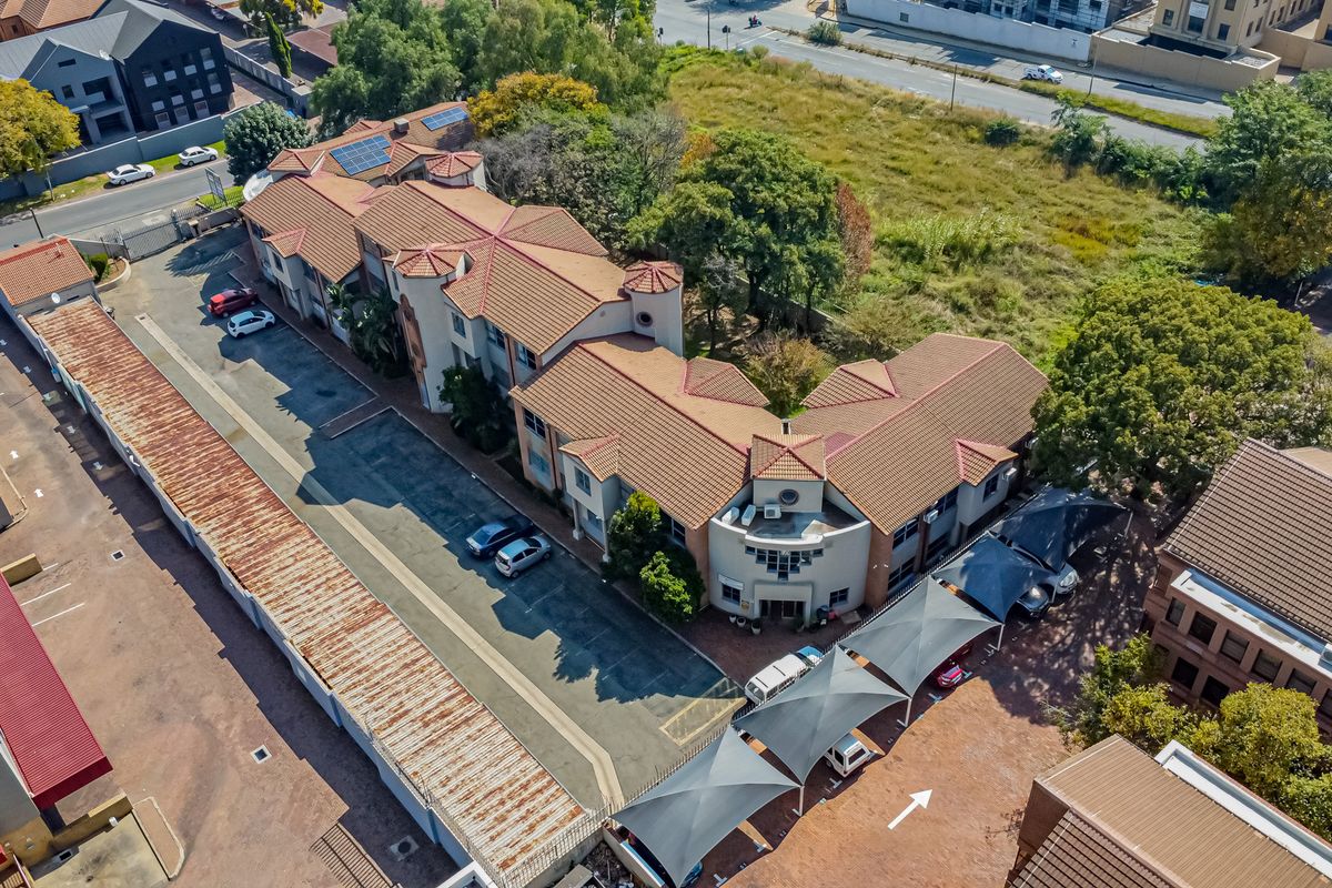 Aerial view of a multi-story office complex featuring a tiled roof, solar panels, paved parking, and shaded carport structures.