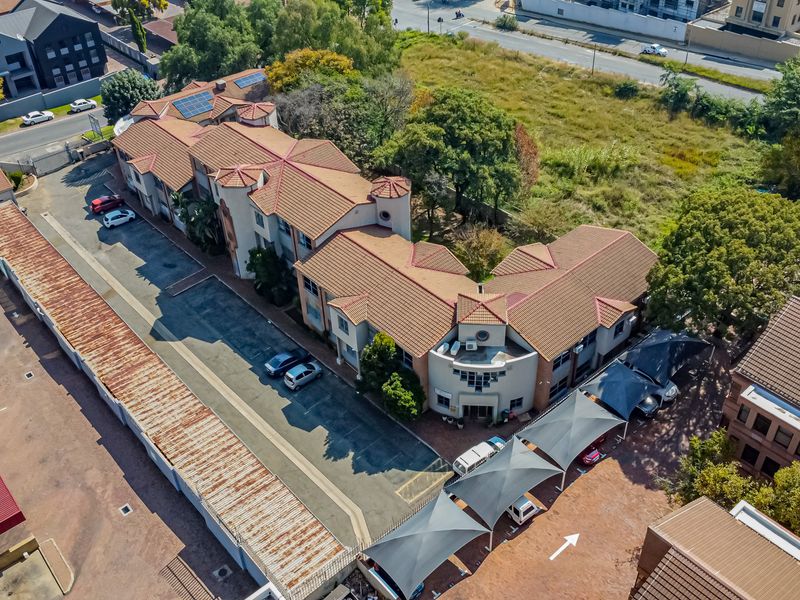 Aerial view of a multi-story office complex featuring a tiled roof, solar panels, paved parking, and shaded carport structures.