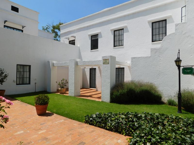 A well-maintained rear courtyard featuring a white stucco facade, a covered pergola, brick paving, and a manicured lawn area.