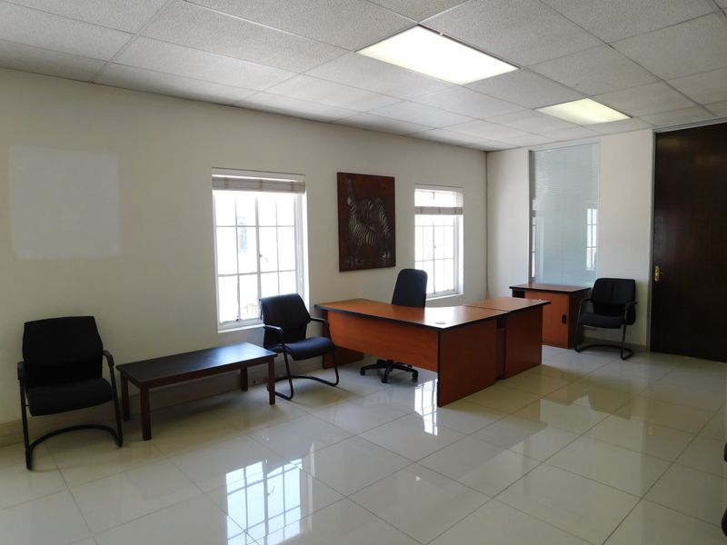 A professional office space featuring polished tiled flooring, a suspended ceiling with recessed lighting, and multiple windows providing natural light.