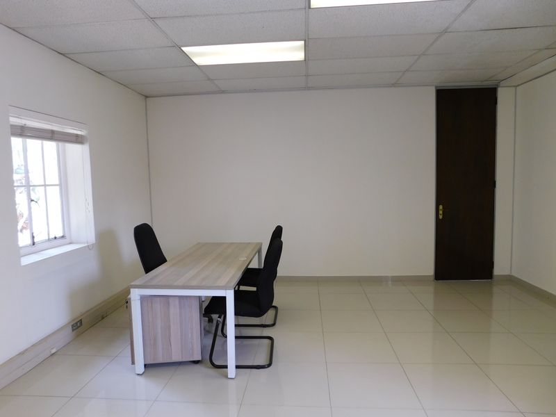 A functional office space featuring tiled flooring, a suspended ceiling with recessed lighting, and a solid timber door.