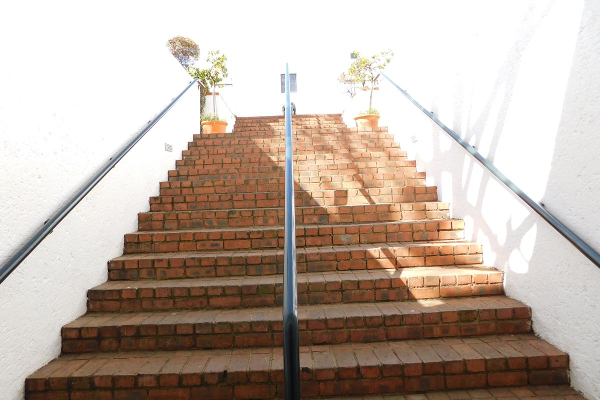 An exterior brick staircase leading to an entrance, featuring metal handrails and white textured side walls.