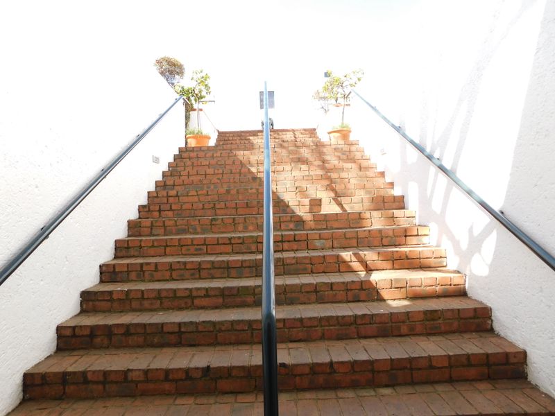 An exterior brick staircase leading to an entrance, featuring metal handrails and white textured side walls.