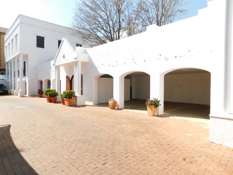 Exterior view of an office building featuring a brick paved driveway and covered parking bays with arched architectural details.