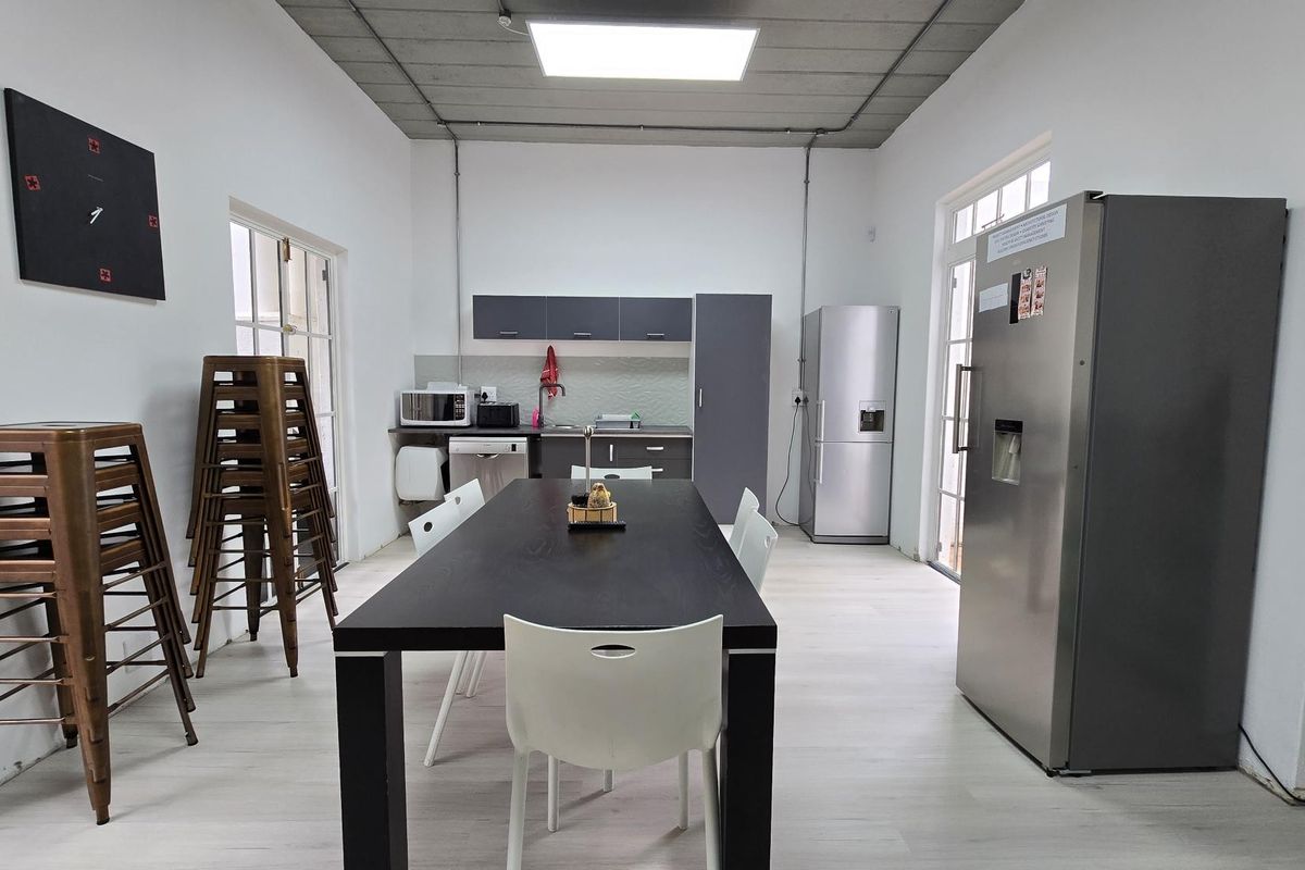 Functional office kitchen area featuring modern cabinetry, laminate flooring, and an industrial-style exposed ceiling with integrated lighting.
