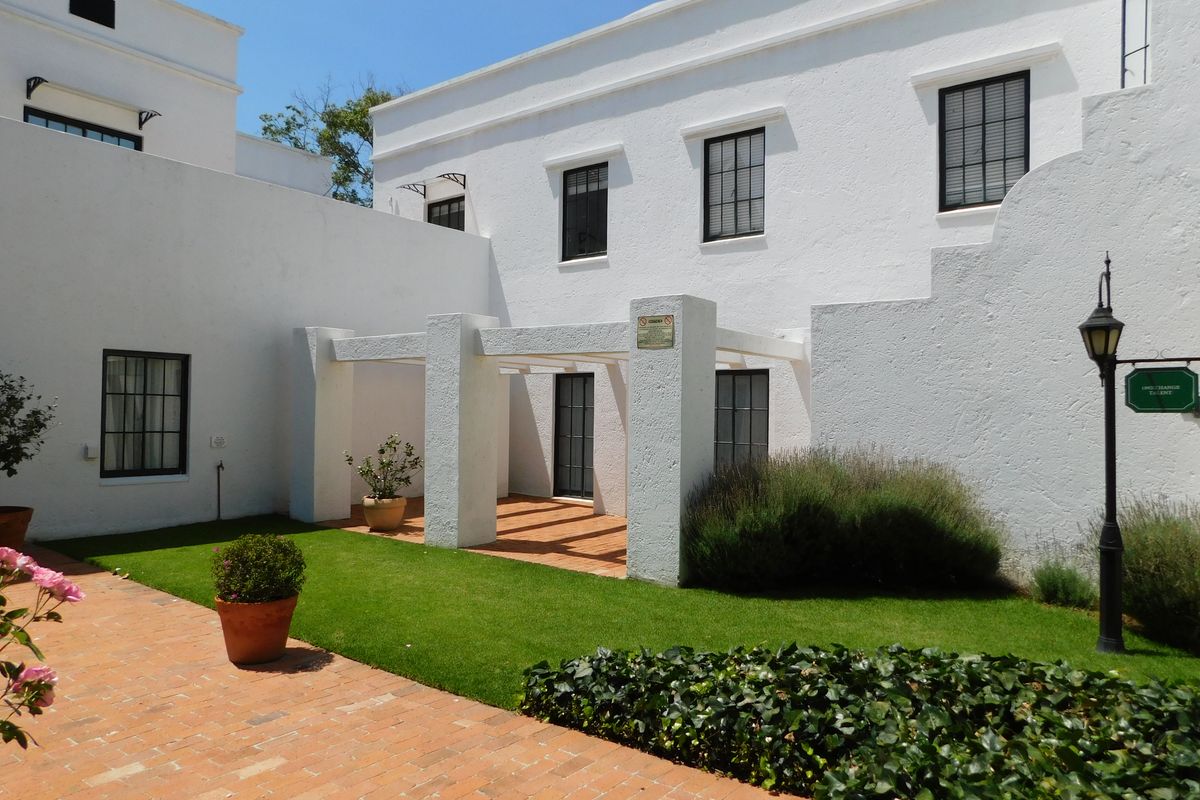 A well-maintained rear courtyard featuring a white stucco facade, a covered pergola, brick paving, and a manicured lawn area.
