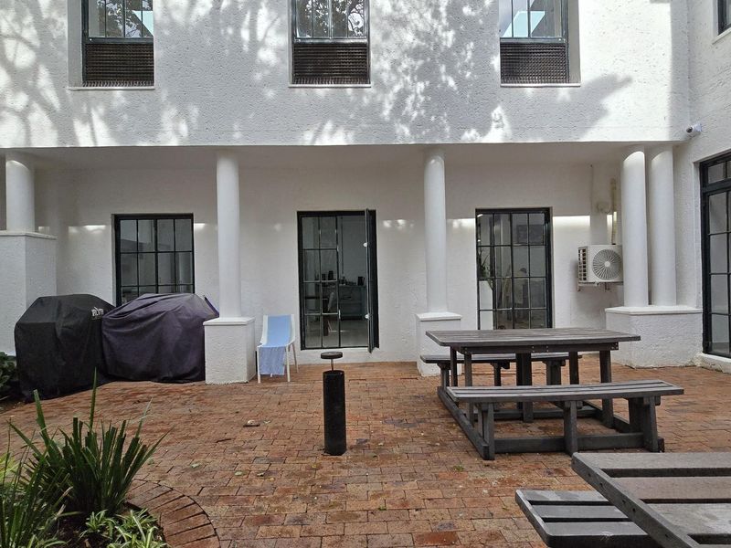 A paved rear courtyard area featuring structural columns, steel-framed windows and doors, and an external air conditioning unit.