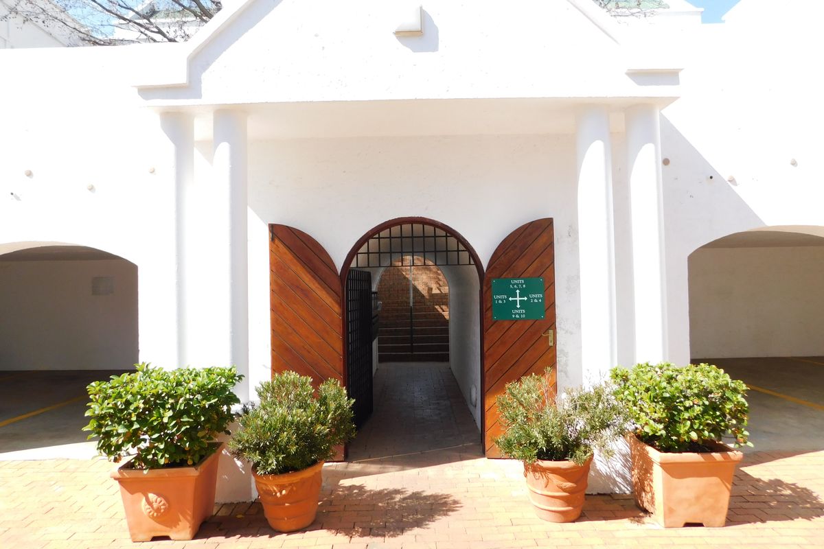 Front entrance of the office complex featuring a classic arched doorway, wooden doors, and covered parking bays on either side.