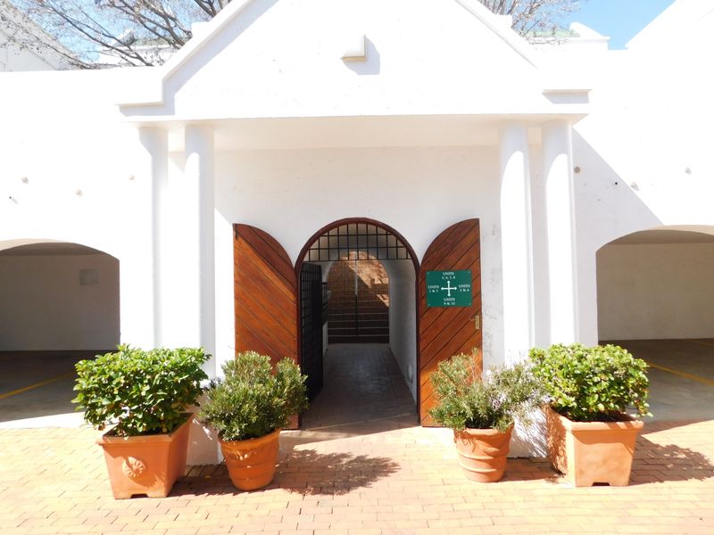 Front entrance of the office complex featuring a classic arched doorway, wooden doors, and covered parking bays on either side.