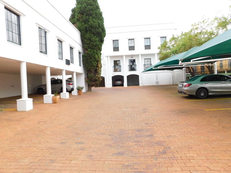 A well-maintained office property exterior featuring a paved courtyard, covered parking bays, and shade cloth carports for convenient vehicle access.