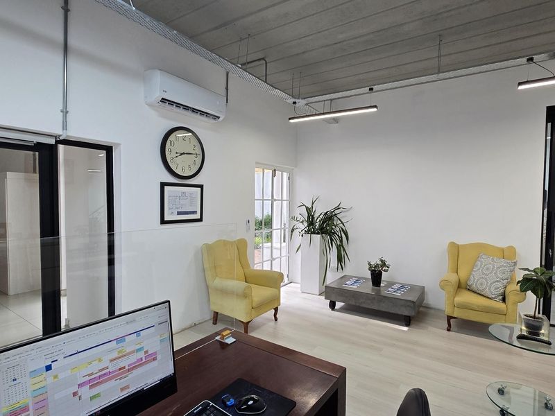 Modern office space featuring an exposed concrete ceiling, linear lighting, air conditioning, and glass partitioning, creating a professional and bright work environment.