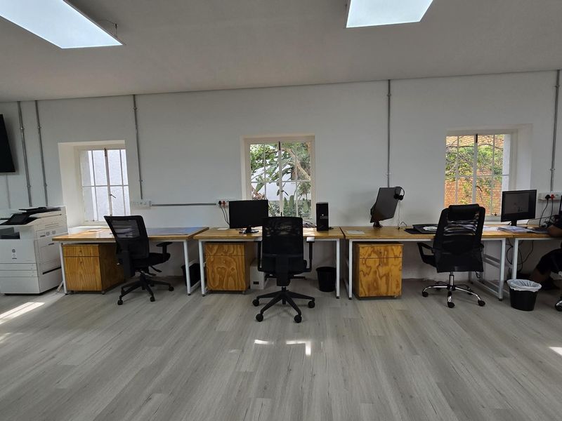 A functional office space featuring light wood-look laminate flooring, recessed ceiling lighting, and multiple workstations with exposed conduit electrical installations.
