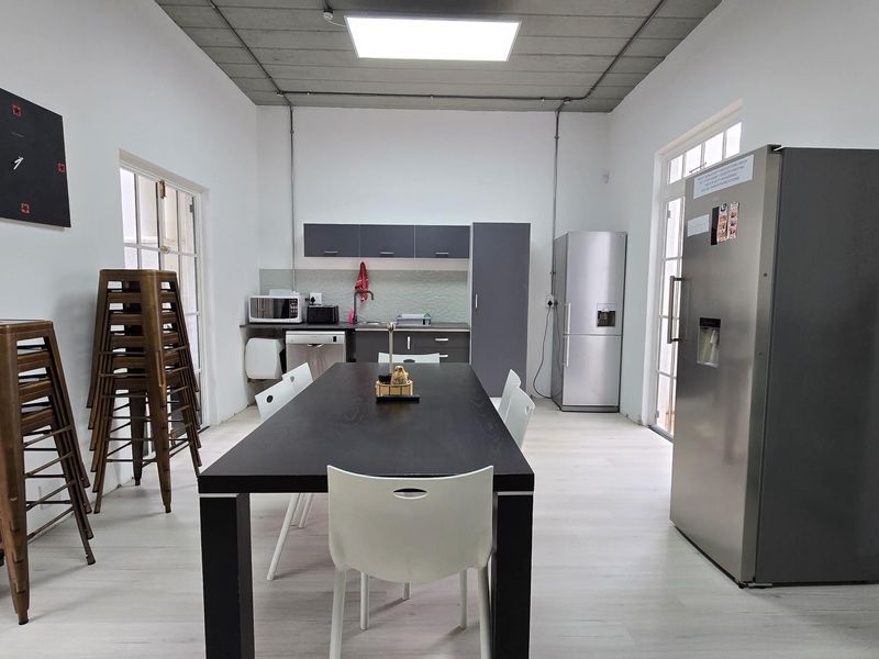 Functional office kitchen area featuring modern cabinetry, laminate flooring, and an industrial-style exposed ceiling with integrated lighting.