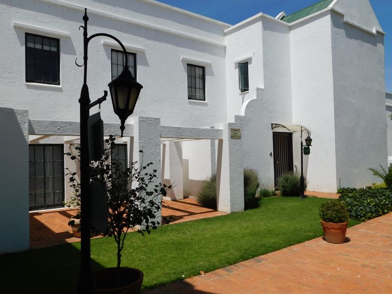 A well-maintained rear exterior view featuring a white facade, a covered pergola area with terracotta paving, and a manicured lawn.