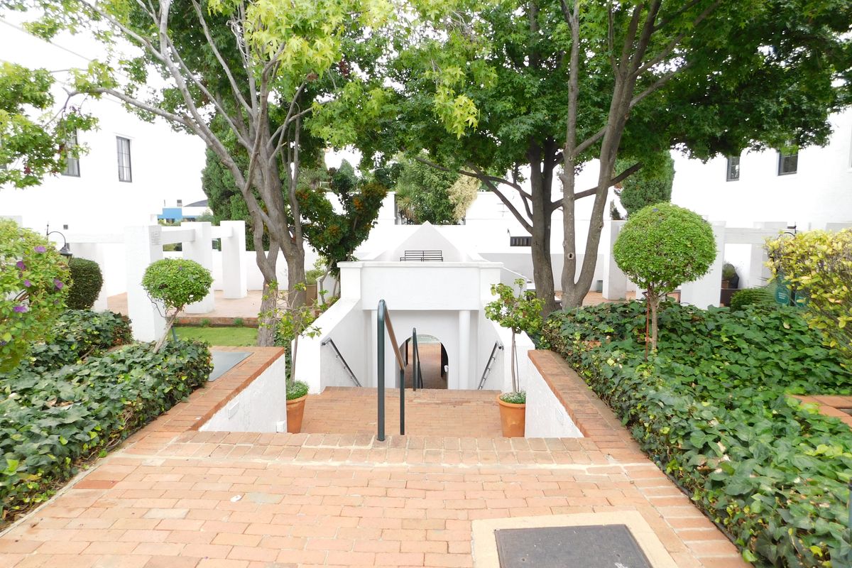 A well-maintained outdoor courtyard area featuring a brick staircase with metal handrails, surrounded by mature trees and landscaped garden beds.