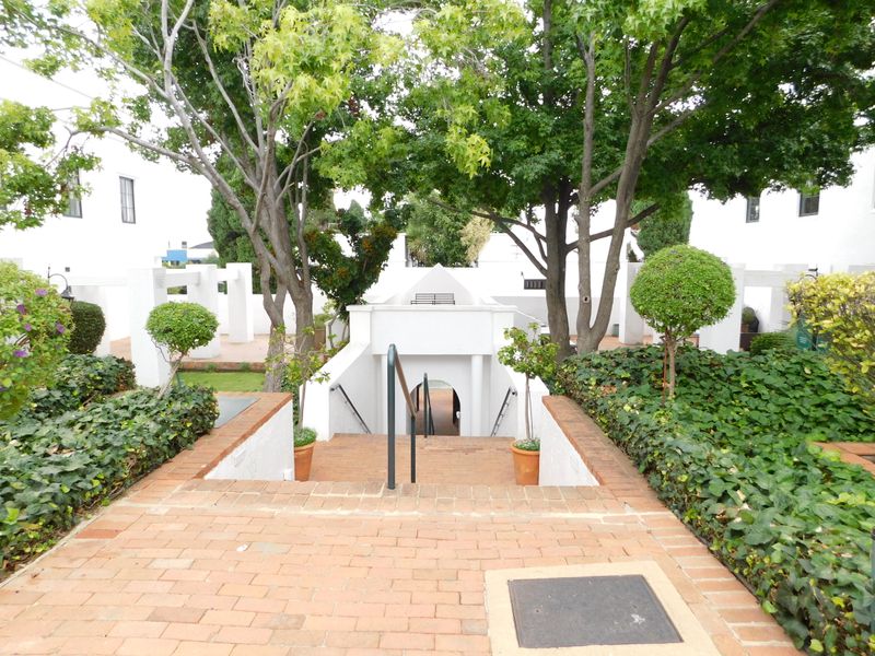A well-maintained outdoor courtyard area featuring a brick staircase with metal handrails, surrounded by mature trees and landscaped garden beds.