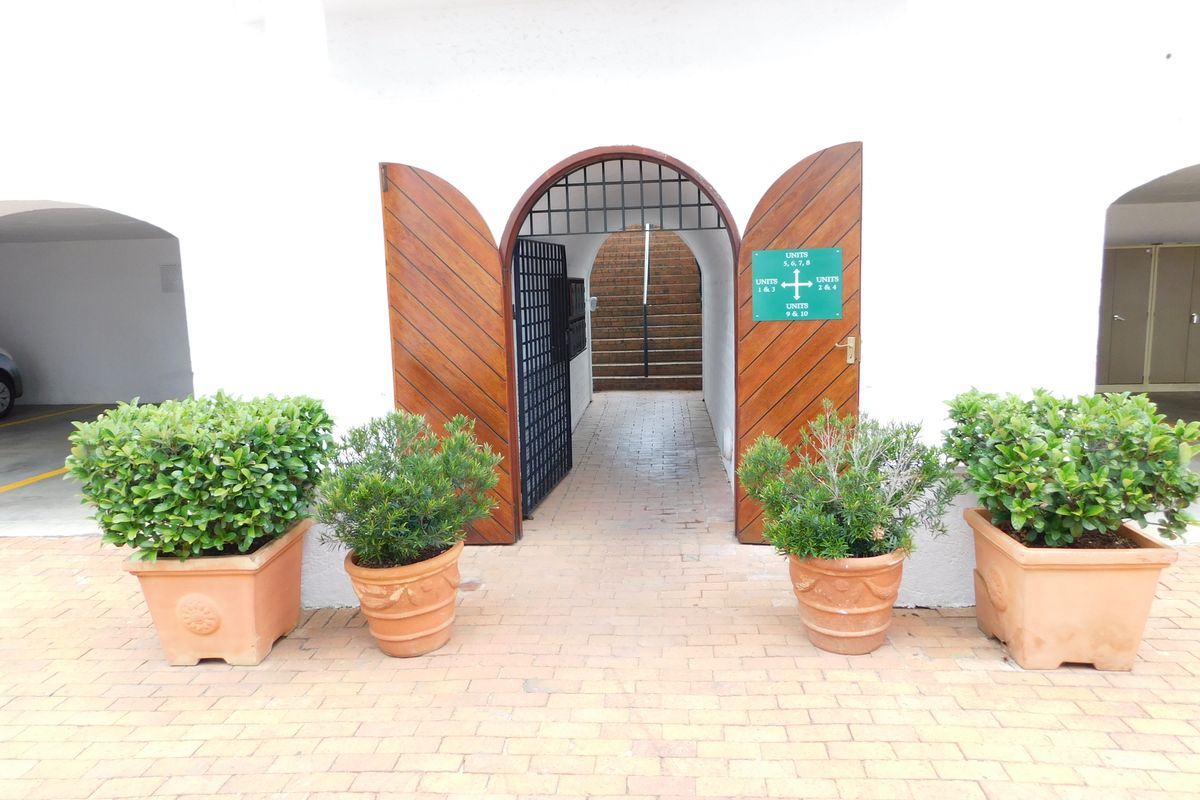 Entrance area featuring arched wooden double doors, brick paving, and directional signage leading to office units.