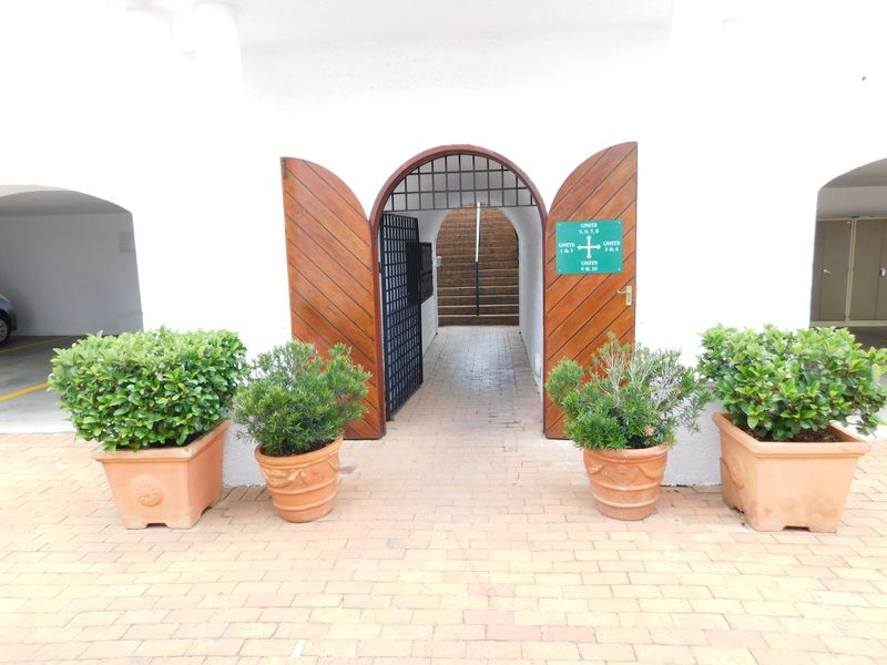 Entrance area featuring arched wooden double doors, brick paving, and directional signage leading to office units.