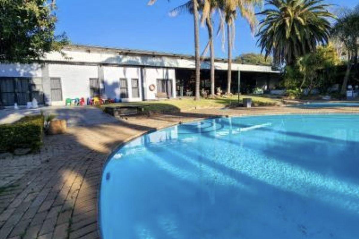 A spacious outdoor pool area featuring a large swimming pool, brick paved surround, and established palm trees set against the lodge building.