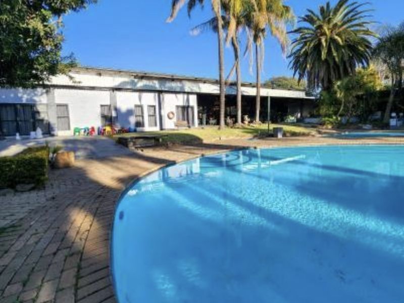 A spacious outdoor pool area featuring a large swimming pool, brick paved surround, and established palm trees set against the lodge building.