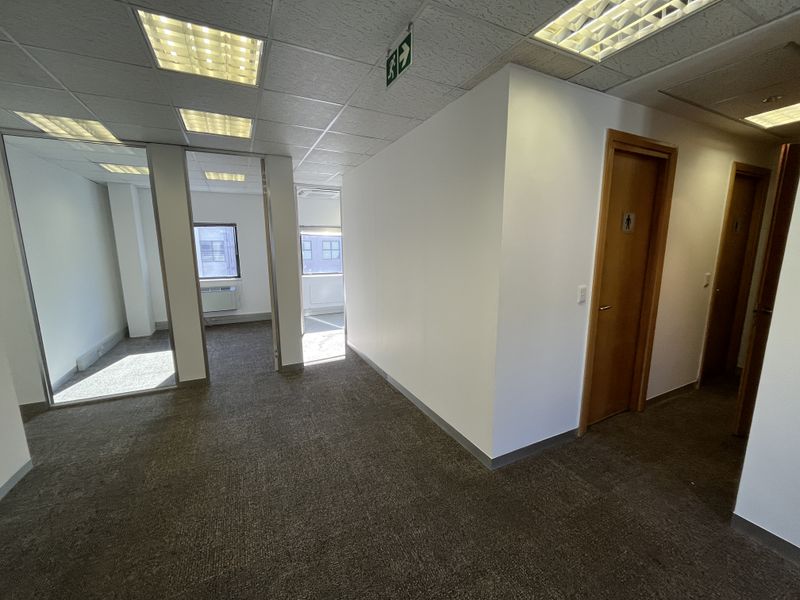 A vacant office space featuring carpeted flooring, suspended ceilings with recessed lighting, glass partitions, and wooden doors leading to private rooms.