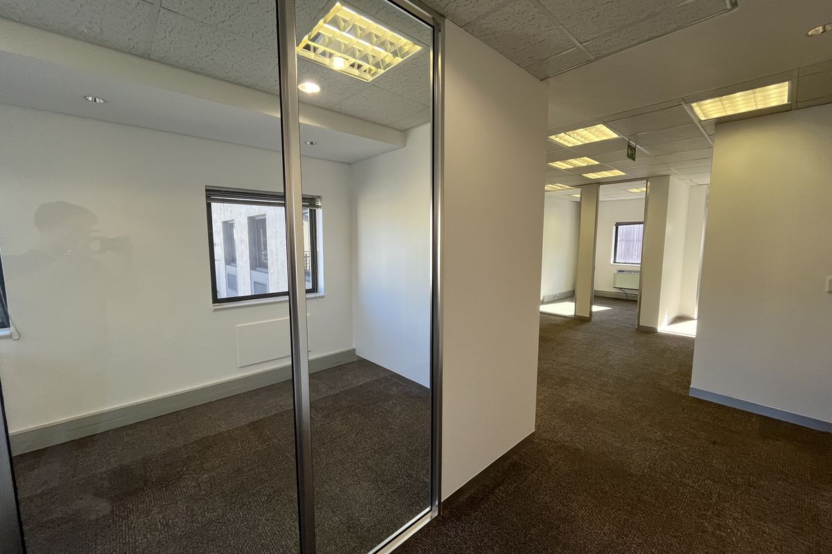 A bright, vacant office space featuring neutral carpeting, suspended ceilings with recessed lighting, and a modern sliding glass partition for flexible workspace configuration.