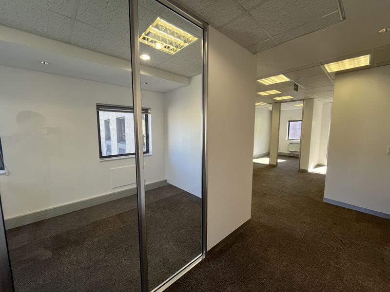 A bright, vacant office space featuring neutral carpeting, suspended ceilings with recessed lighting, and a modern sliding glass partition for flexible workspace configuration.