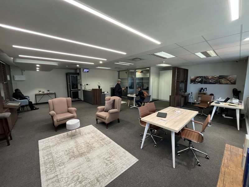 A spacious, well-lit modern office environment featuring recessed linear lighting, carpeted flooring, and a professional reception area with glass partitions.