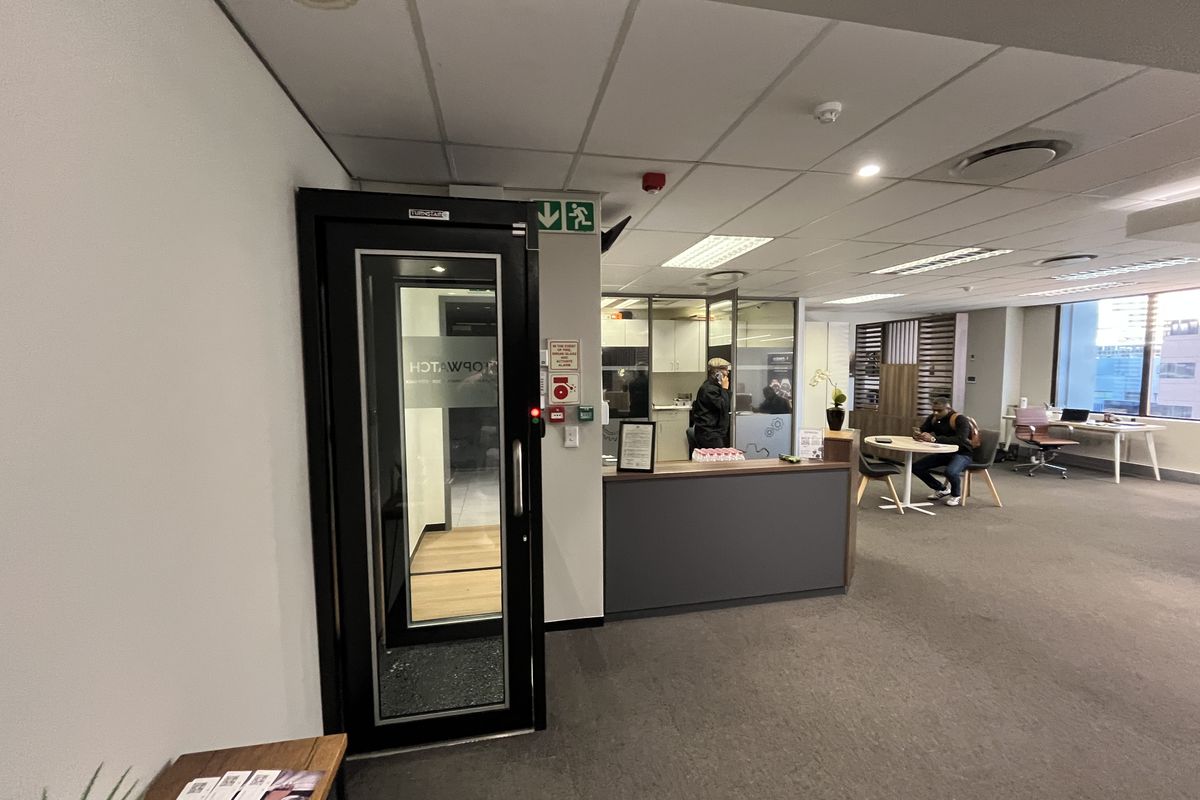 Open-plan office space featuring a reception area, secure access door, suspended ceiling with recessed lighting, and glass-partitioned office rooms.