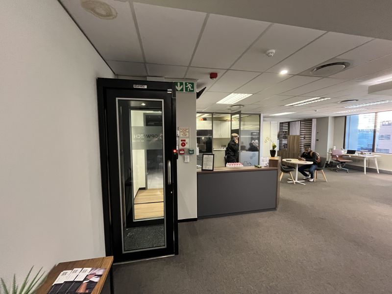 Open-plan office space featuring a reception area, secure access door, suspended ceiling with recessed lighting, and glass-partitioned office rooms.