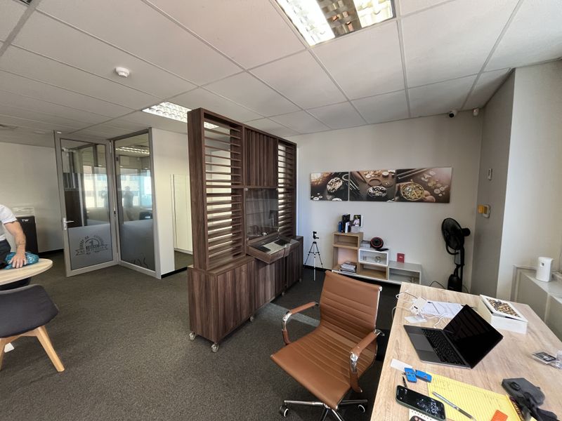 A professional office space featuring a glass partition, suspended ceiling with recessed lighting, and a built-in wooden room divider.