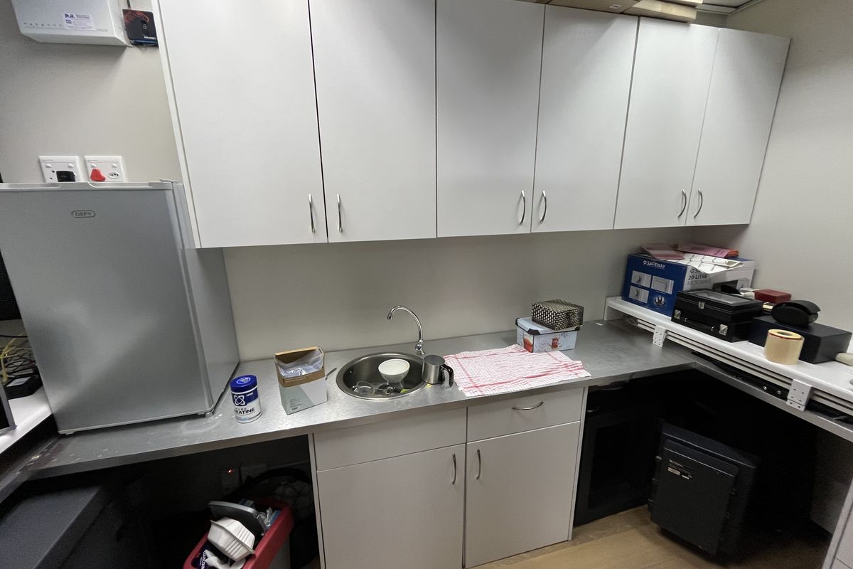 A compact office kitchenette featuring white cabinetry, a stainless steel countertop, and a small sink area.