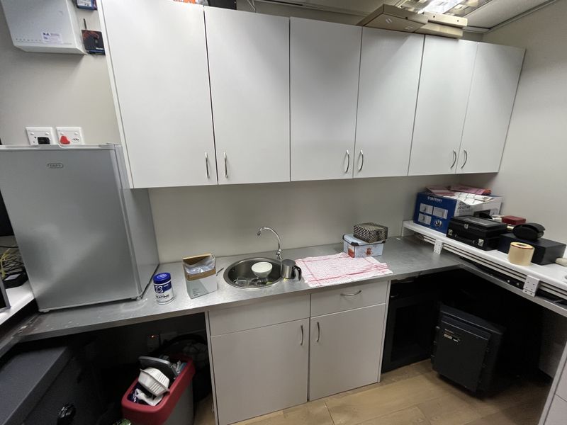 A compact office kitchenette featuring white cabinetry, a stainless steel countertop, and a small sink area.