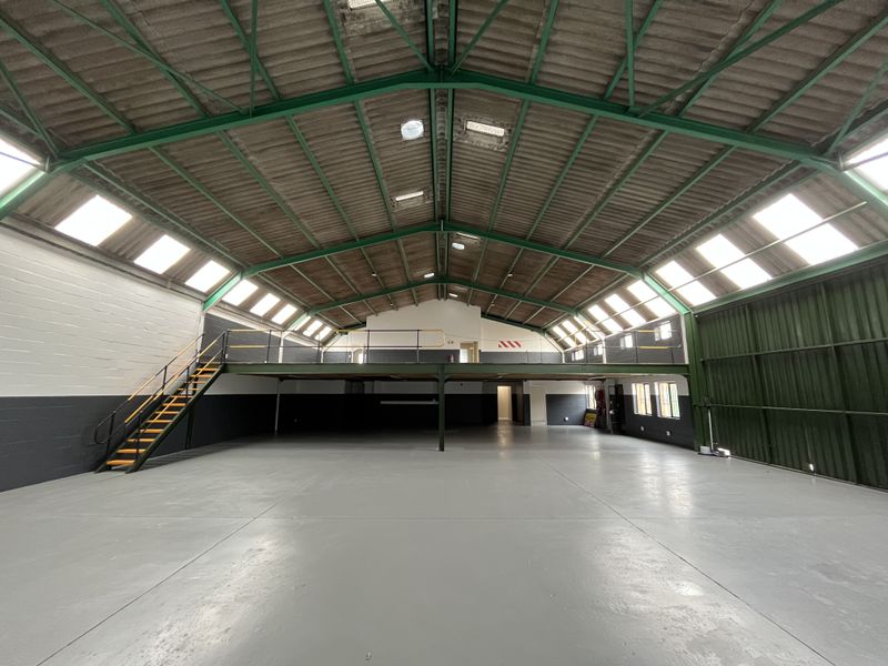 Spacious industrial warehouse unit featuring a mezzanine level, steel staircase, high ceilings with skylights, and durable epoxy-coated concrete flooring.